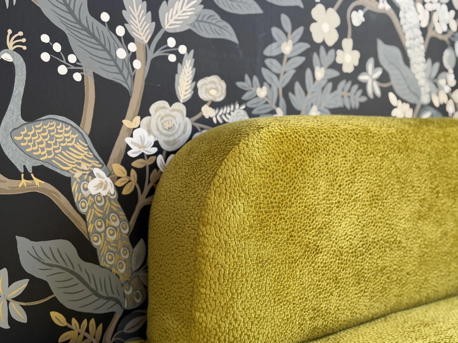 Rounded green upholstered back against botanical wallpaper