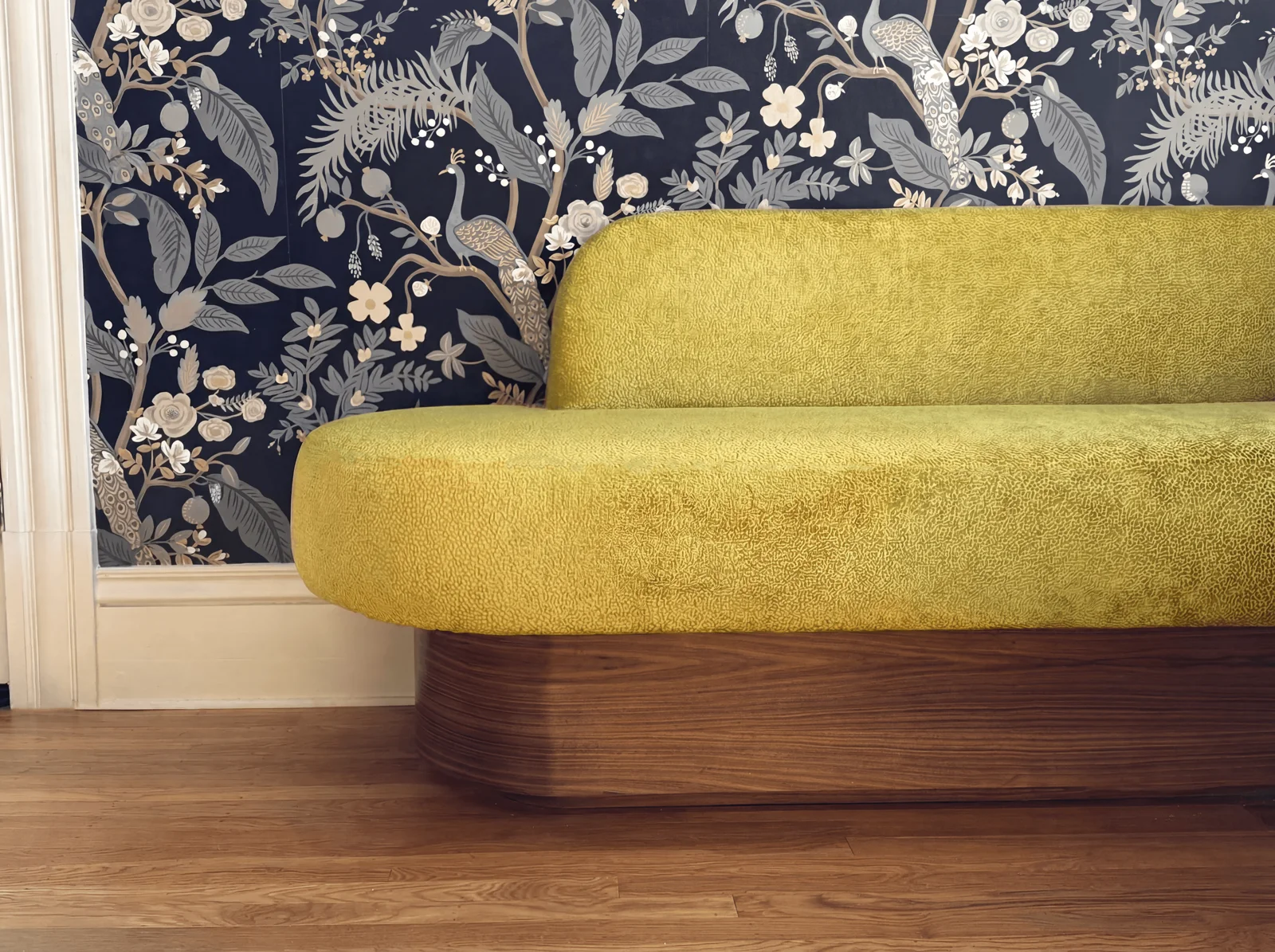 Curved green upholstered seating with a wood base against botanical wallpaper
