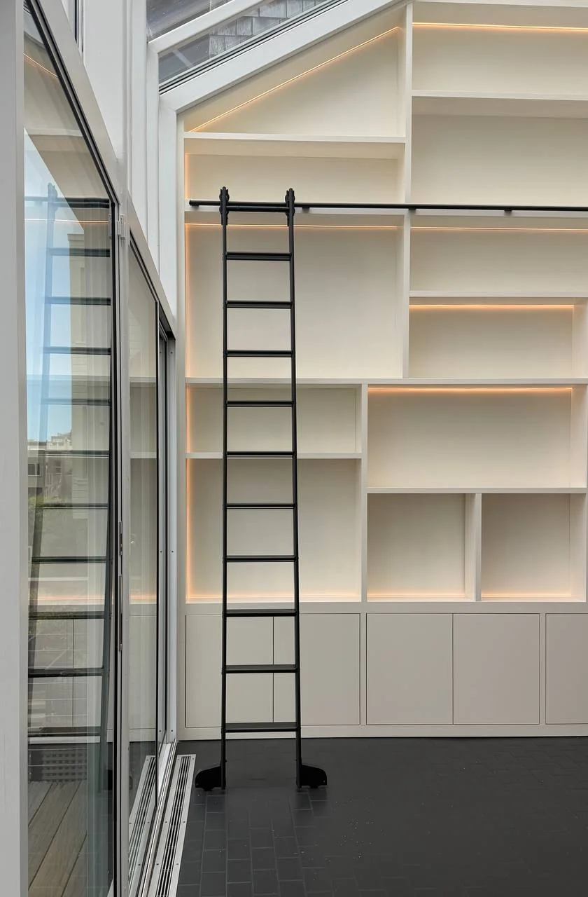 The rolling ladder on its rail against lit shelves and closed base cabinets