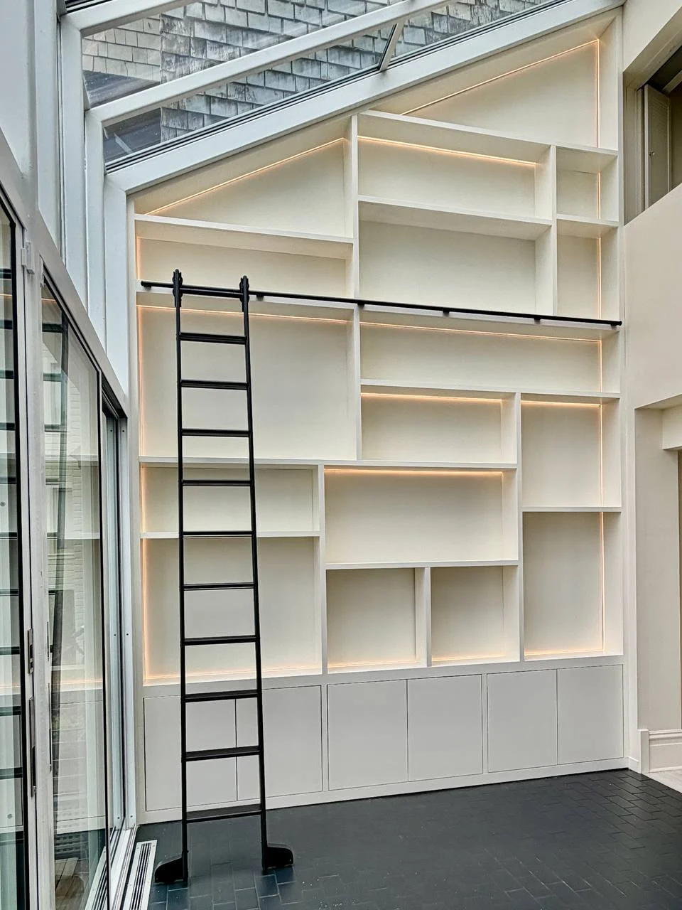 The full shelving wall, lit from within, following the sloping glass roof