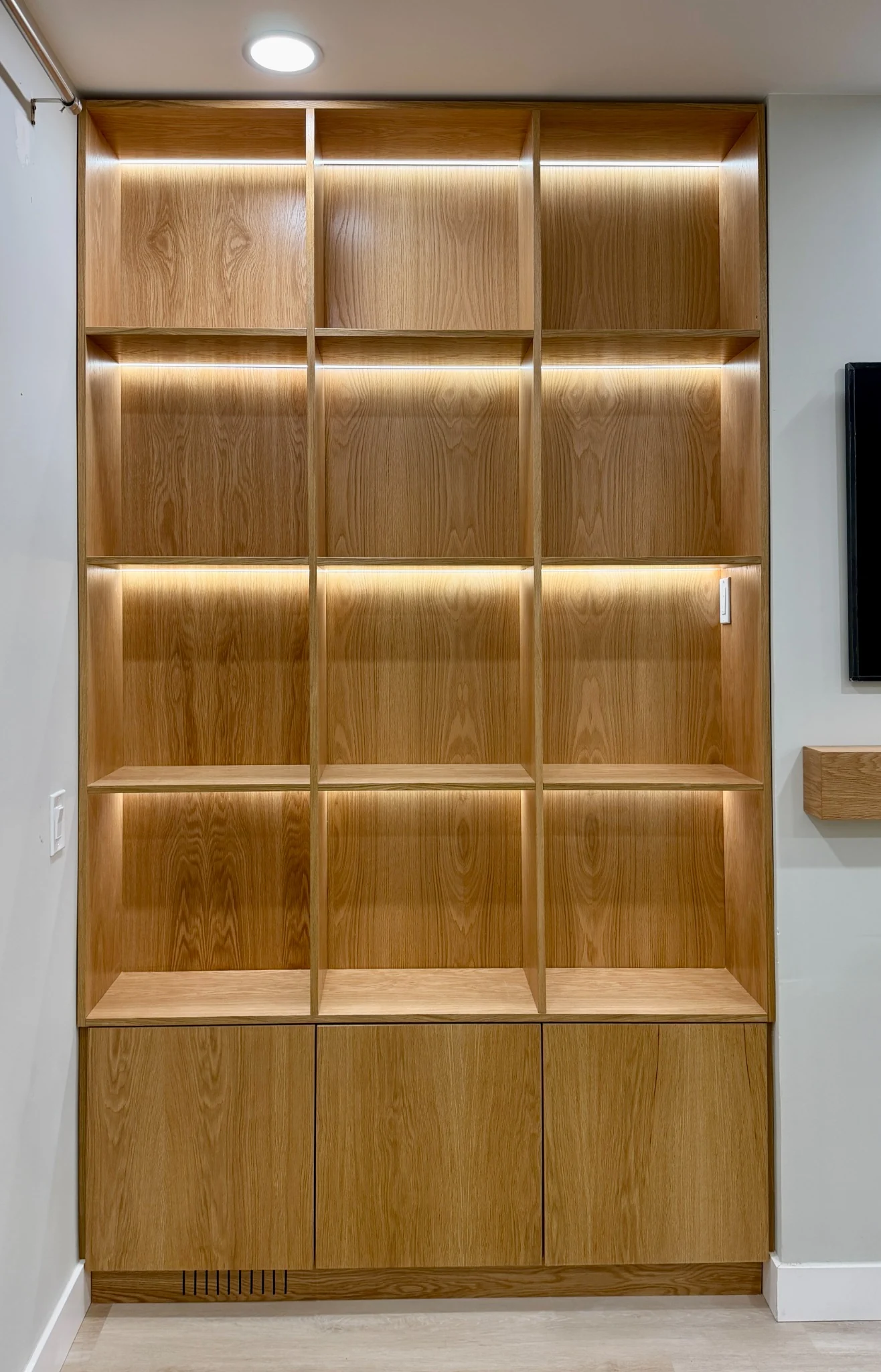 Full-height golden wood-grain shelving with three illuminated bays and closed lower cabinets