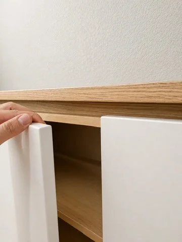 A hand opening a pale cabinet door beneath the wood top