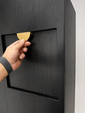 Hand opening the dark cabinet using a half-circle pull