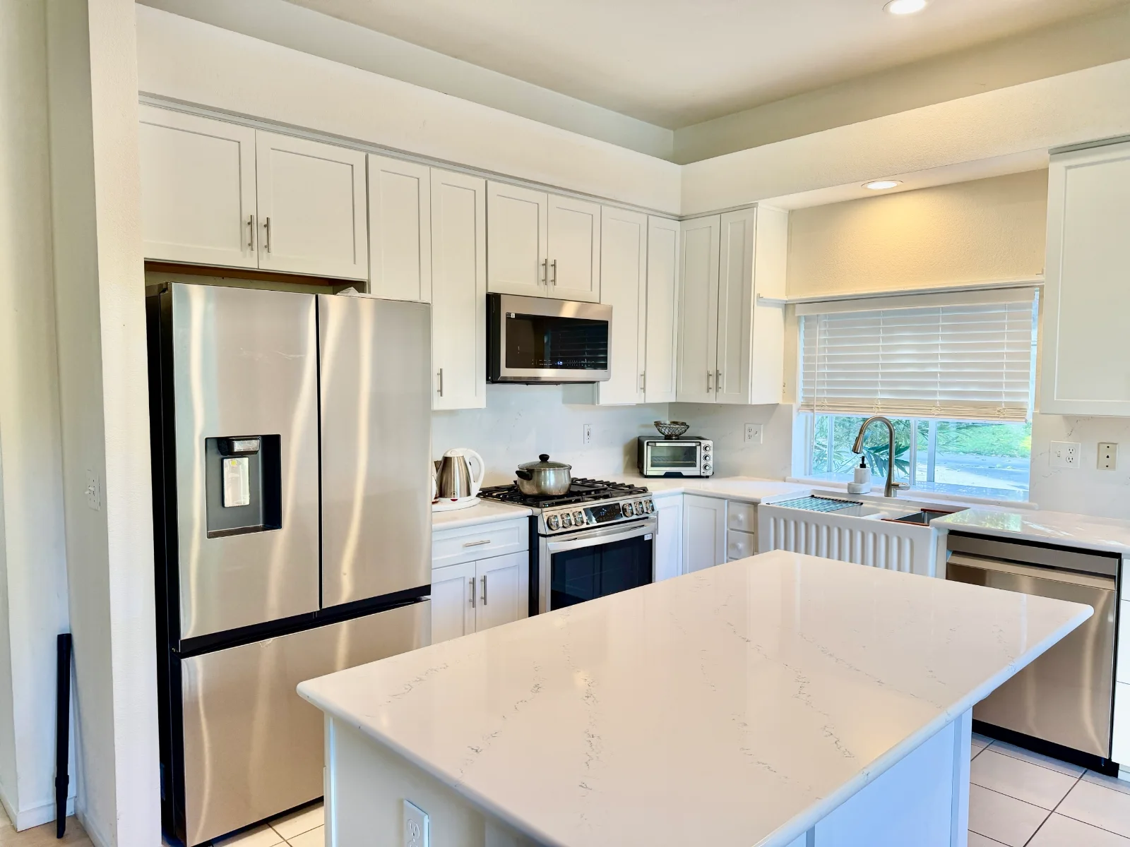 White shaker kitchen with upper cabinets, stainless appliances, and a quartz island