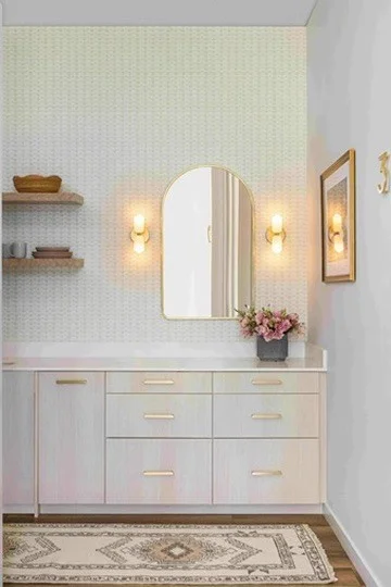 Pale vanity cabinetry with drawers, metallic pulls, and an arched mirror